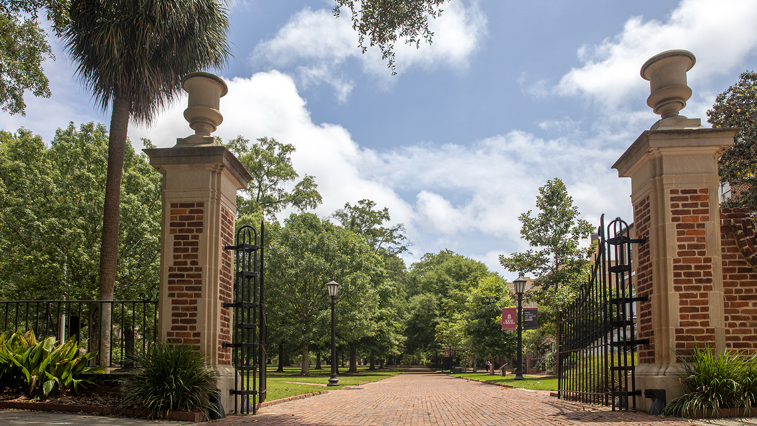 Brick pillars begin a horseshoe-shaped gate at the University of South Carolina. Trees surround the pillars.